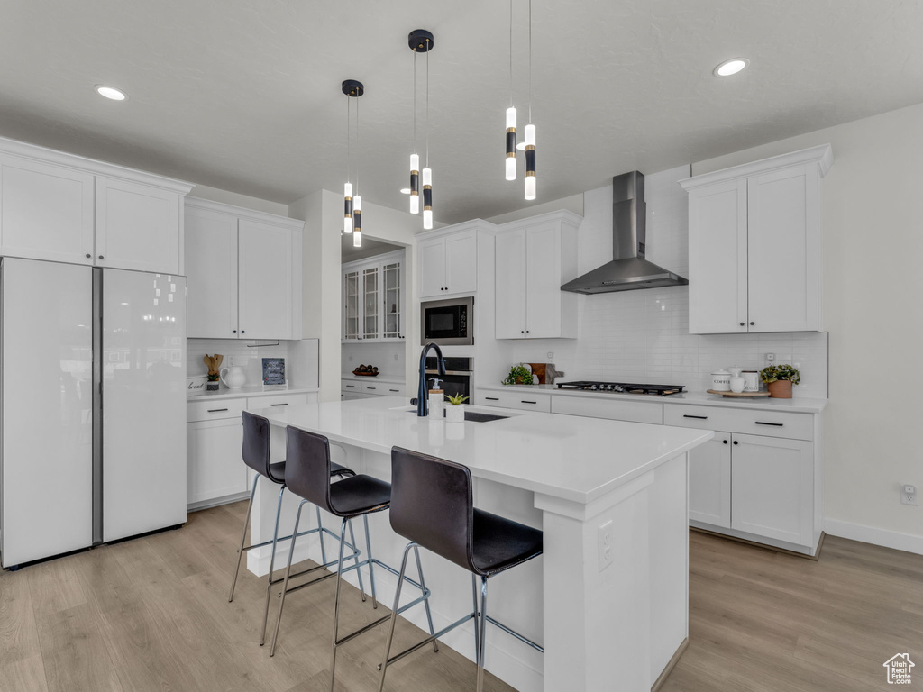 Kitchen with wall chimney range hood, white fridge, built in microwave, a sink, and light wood-style floors