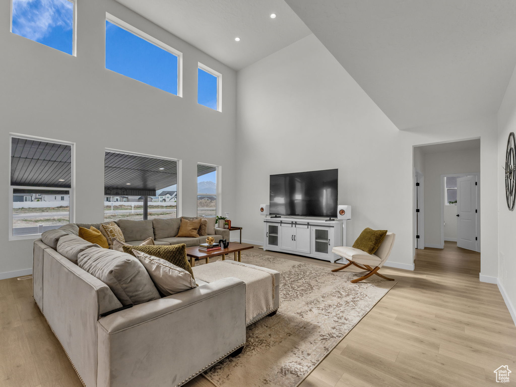 Living area with a high ceiling, light wood-type flooring, plenty of natural light, and baseboards