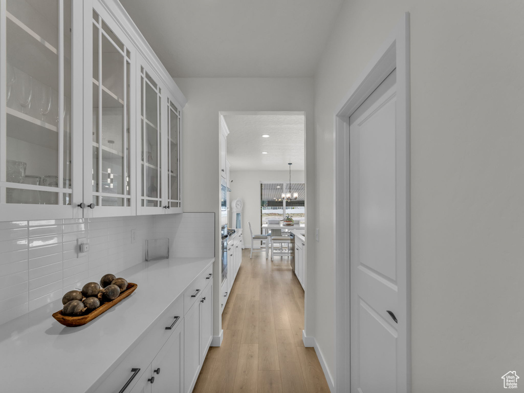 Kitchen featuring decorative backsplash, white cabinets, light countertops, light wood finished floors, and glass insert cabinets