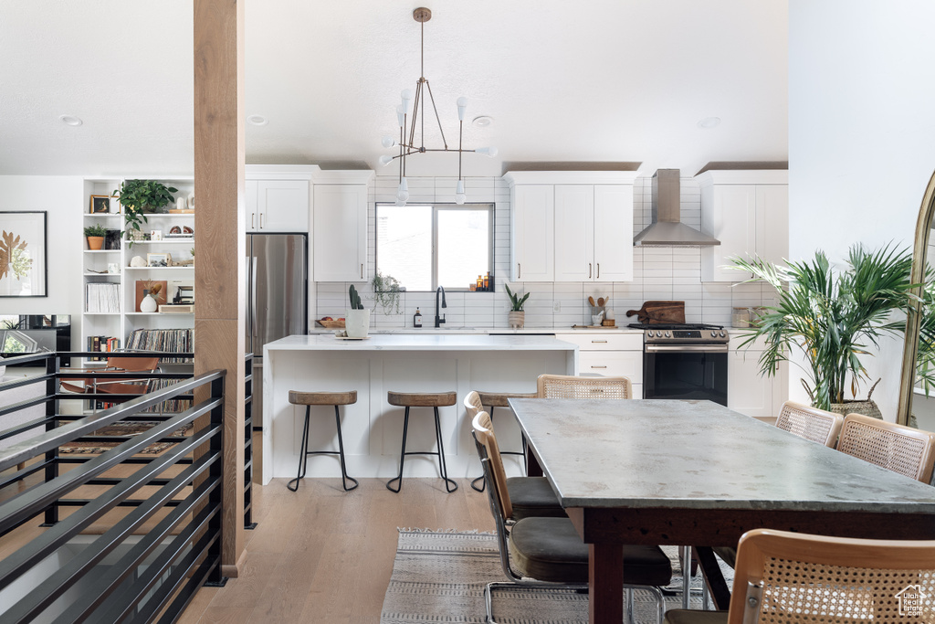 Kitchen featuring wall chimney range hood, stainless steel range oven, white cabinets, and tasteful backsplash