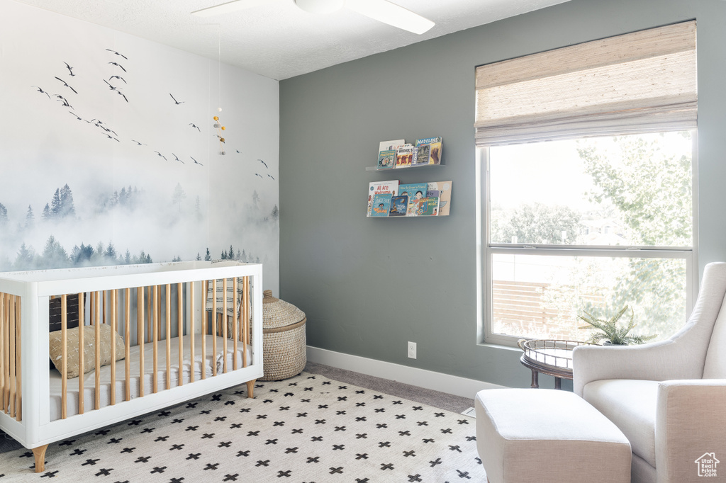 Bedroom featuring a nursery area, carpet floors, baseboards, and a ceiling fan
