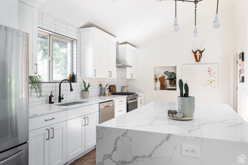 Kitchen with appliances with stainless steel finishes, a sink, wall chimney exhaust hood, tasteful backsplash, and white cabinets