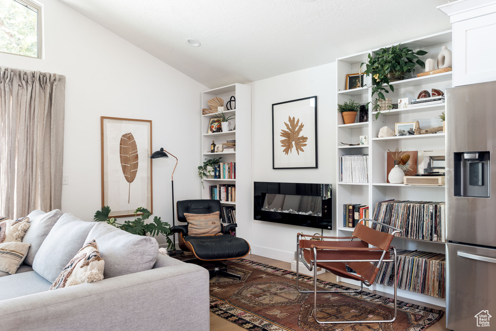 Living area featuring vaulted ceiling, wood finished floors, and a glass covered fireplace