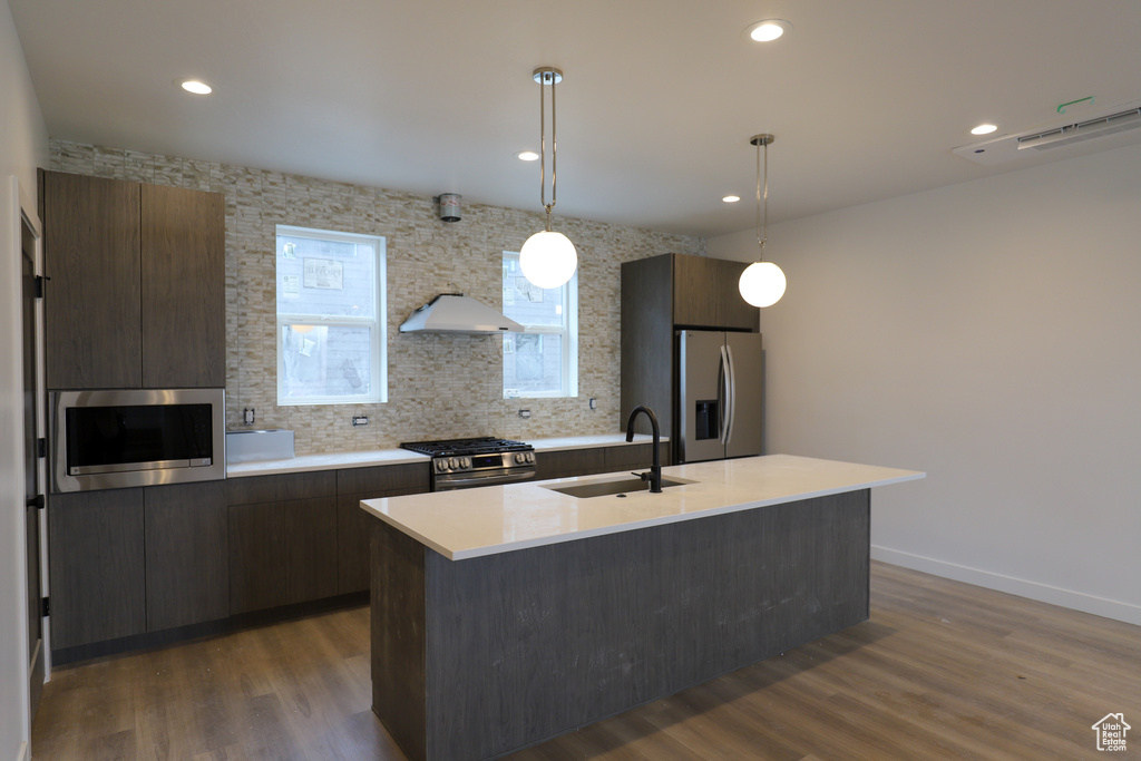 Kitchen featuring a sink, stainless steel appliances, light countertops, modern cabinets, and a kitchen island with sink