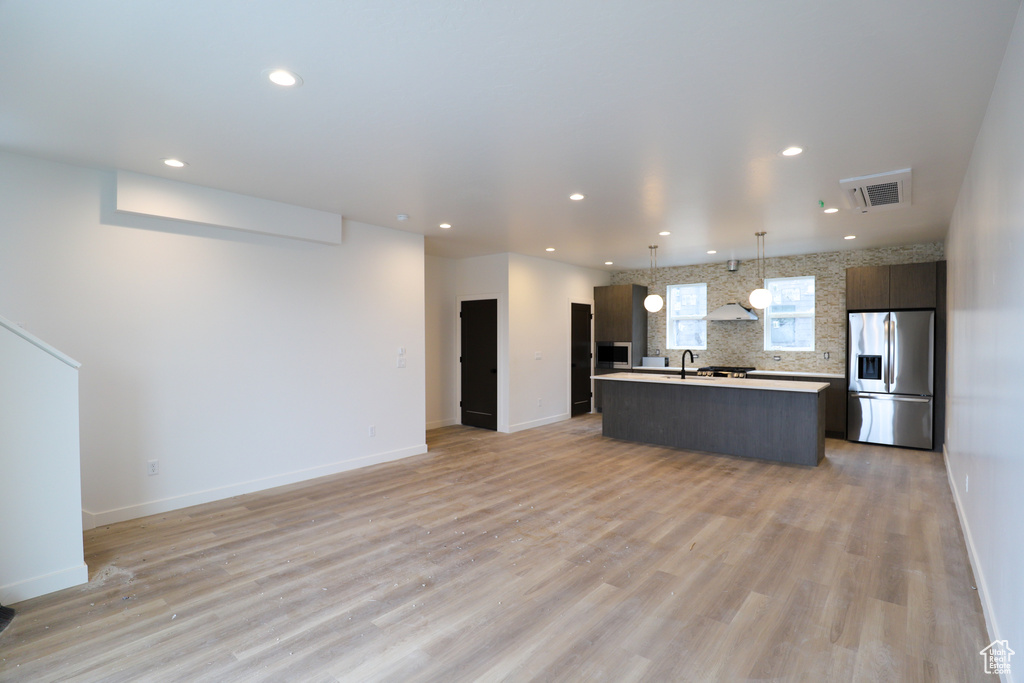 Kitchen featuring stainless steel fridge, open floor plan, a kitchen island with sink, light countertops, and recessed lighting