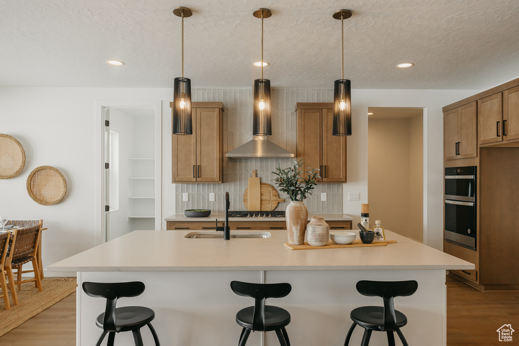 Kitchen featuring wall chimney range hood, a sink, light wood-style floors, decorative backsplash, and recessed lighting