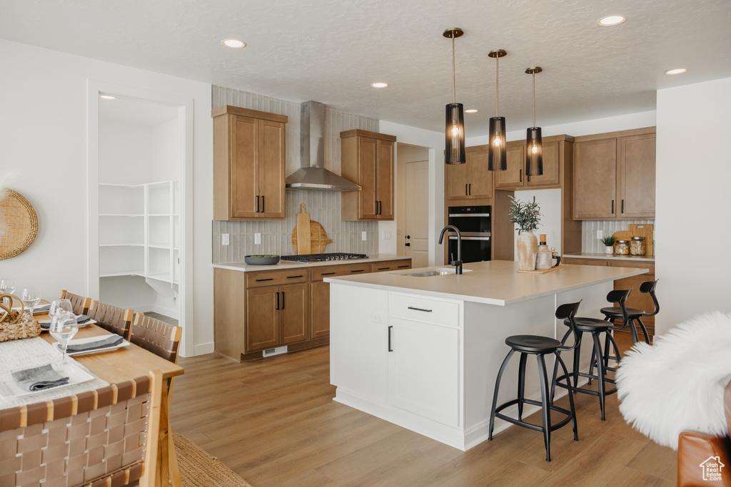 Kitchen featuring wall chimney range hood, a sink, a breakfast bar area, decorative backsplash, and recessed lighting