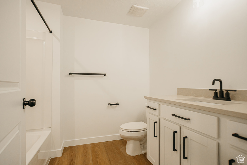 Full bath featuring vanity, wood finished floors, toilet, bathtub / shower combination, and baseboards