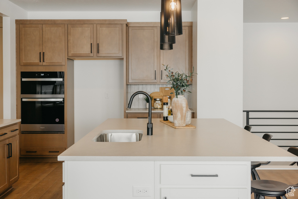 Kitchen with double oven, a sink, light countertops, dark wood-type flooring, and a breakfast bar area