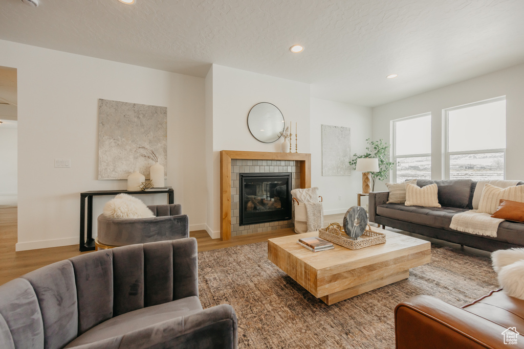 Living area with wood finished floors, a tiled fireplace, recessed lighting, and baseboards