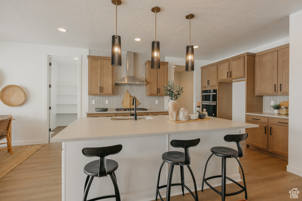 Kitchen featuring wall chimney range hood, backsplash, a sink, a kitchen bar, and recessed lighting