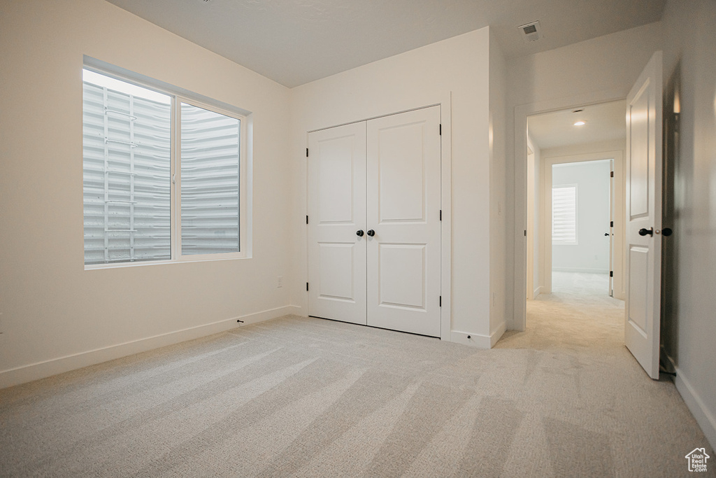 Unfurnished bedroom with light colored carpet, multiple windows, and baseboards