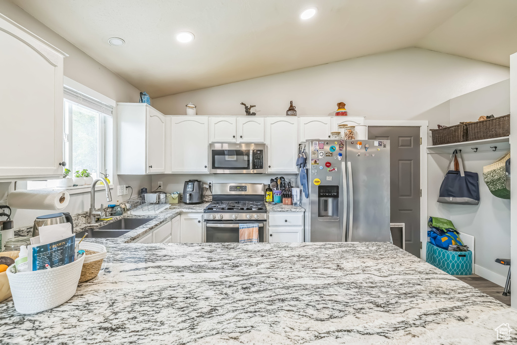 Kitchen with appliances with stainless steel finishes, a sink, lofted ceiling, light stone counters, and white cabinetry