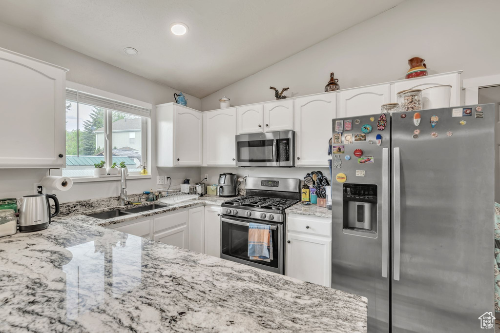 Kitchen featuring appliances with stainless steel finishes, light stone countertops, white cabinetry, vaulted ceiling, and recessed lighting