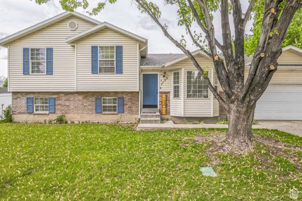 Tri-level home with a front lawn, brick siding, and an attached garage