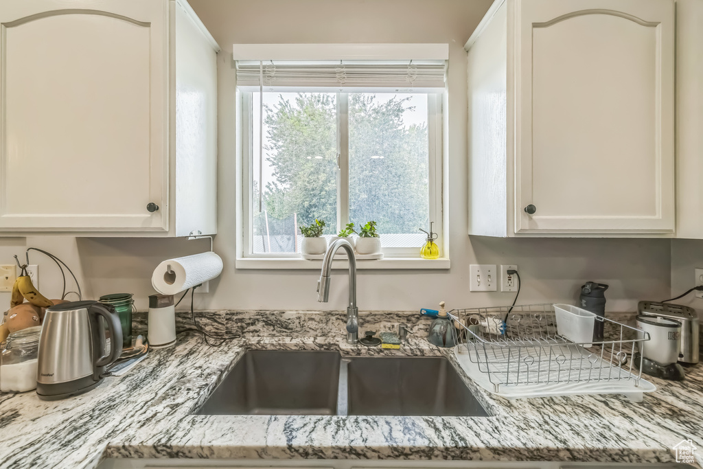 Kitchen featuring a sink, white cabinets, and light stone countertops
