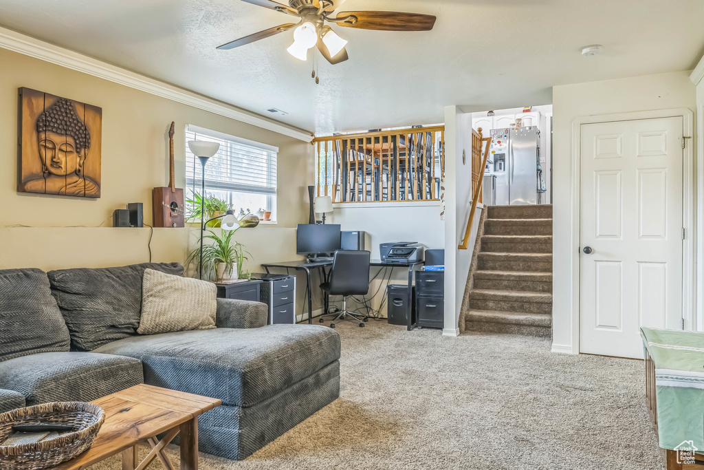 Carpeted living room featuring crown molding, a ceiling fan, stairway, and a desk