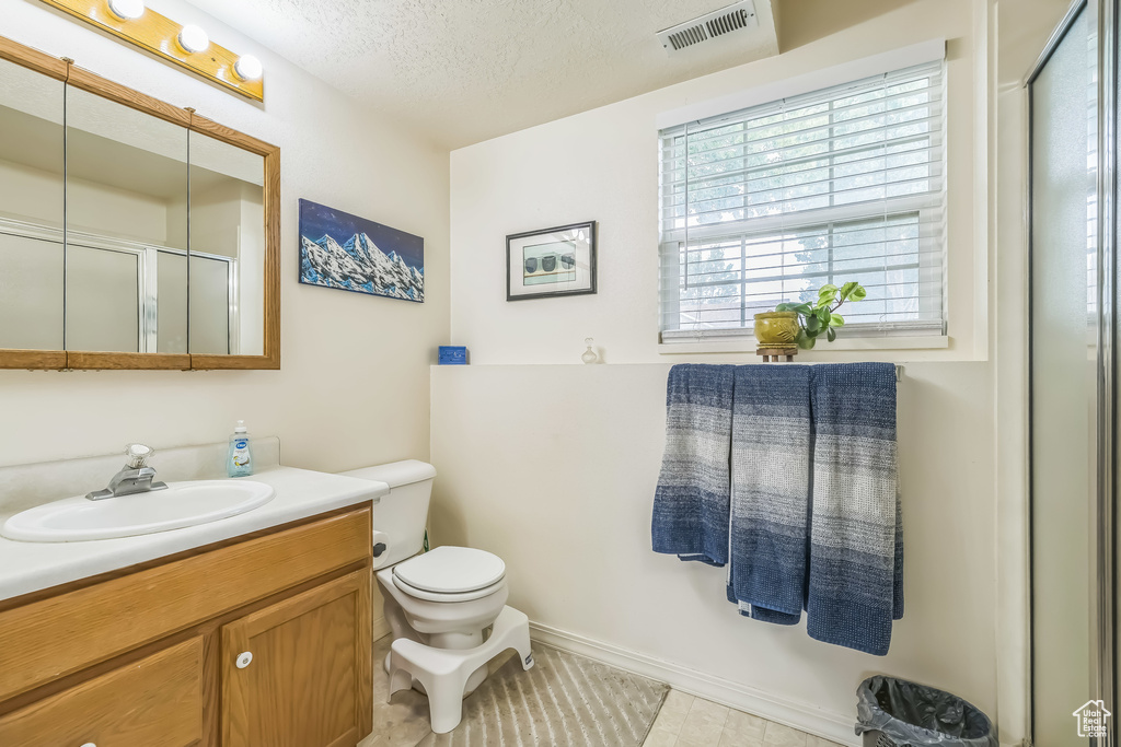 Bathroom with toilet, vanity, a textured ceiling, a shower with door, and tile patterned floors