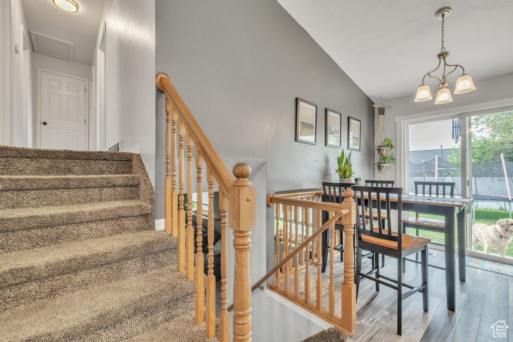 Staircase featuring wood finished floors, vaulted ceiling, and a chandelier