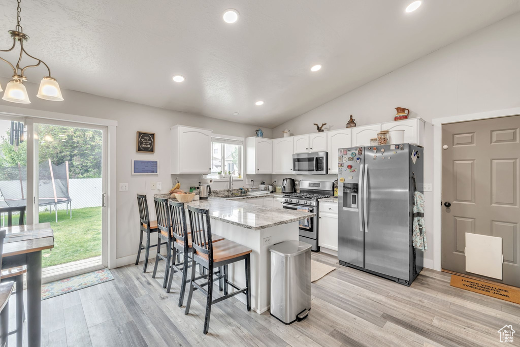 Kitchen with appliances with stainless steel finishes, a peninsula, a breakfast bar, white cabinets, and recessed lighting