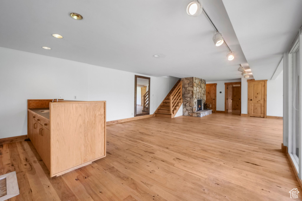Unfurnished living room with light wood-type flooring, baseboards, stairway, and a stone fireplace