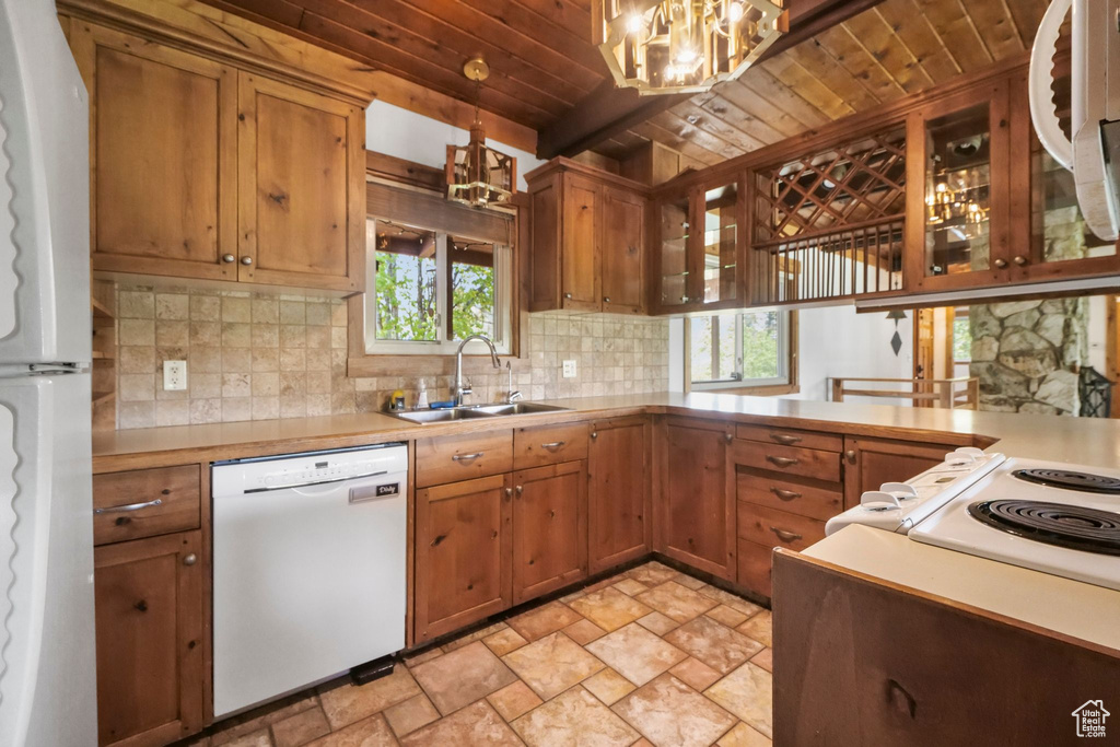 Kitchen featuring white appliances, a chandelier, a sink, wooden ceiling with exposed beams, and light stone finish floors