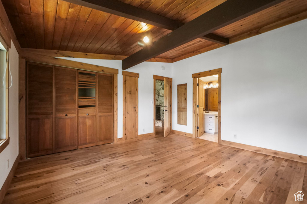 Unfurnished bedroom with light wood-style flooring, baseboards, multiple closets, wooden ceiling with exposed beams, and connected bathroom