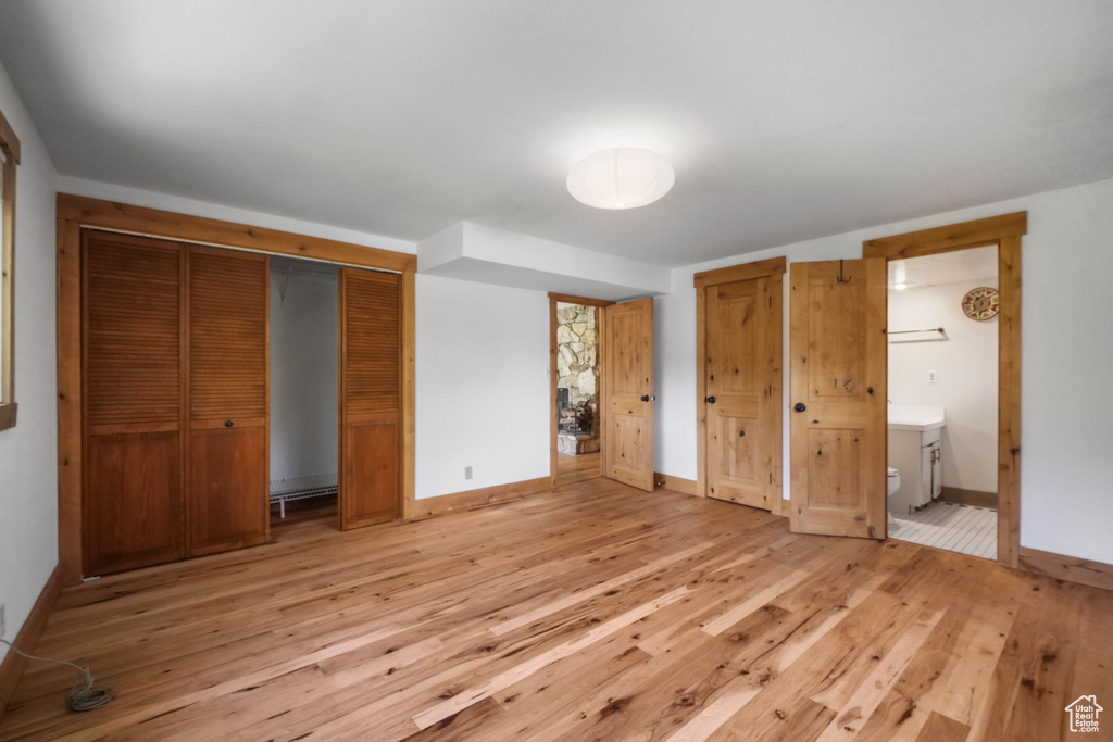 Unfurnished bedroom with light wood-type flooring, baseboards, connected bathroom, and multiple closets