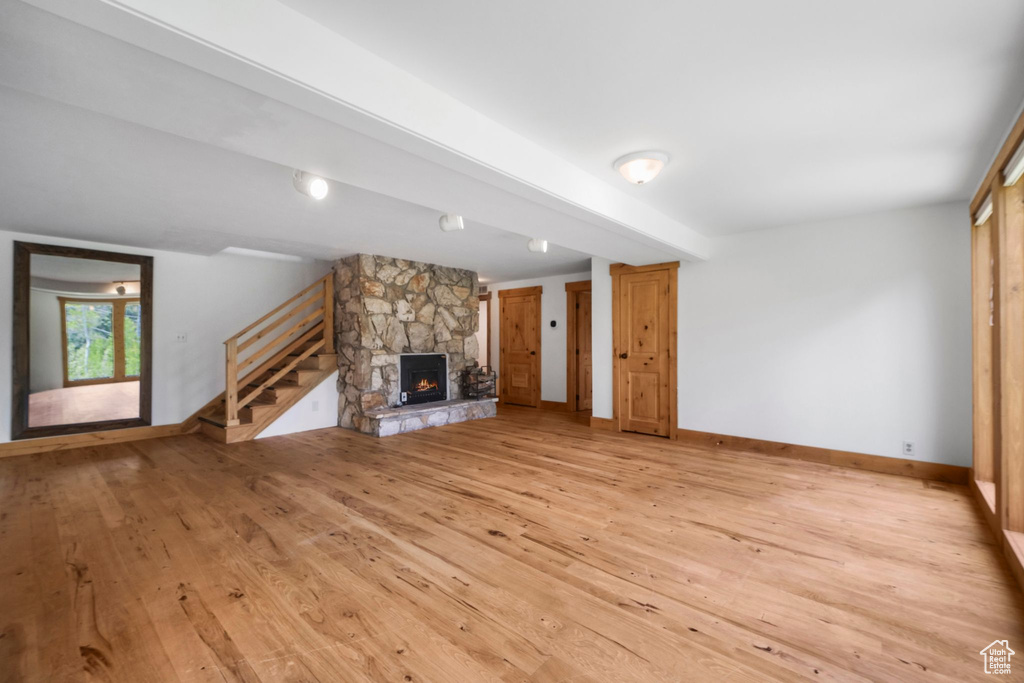Unfurnished living room featuring light wood-type flooring, a stone fireplace, stairs, and baseboards