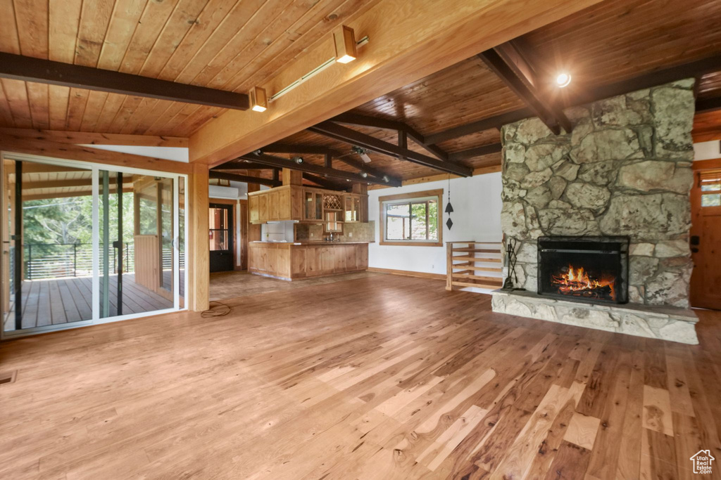 Unfurnished living room featuring wood ceiling, hardwood / wood-style floors, a stone fireplace, and baseboards