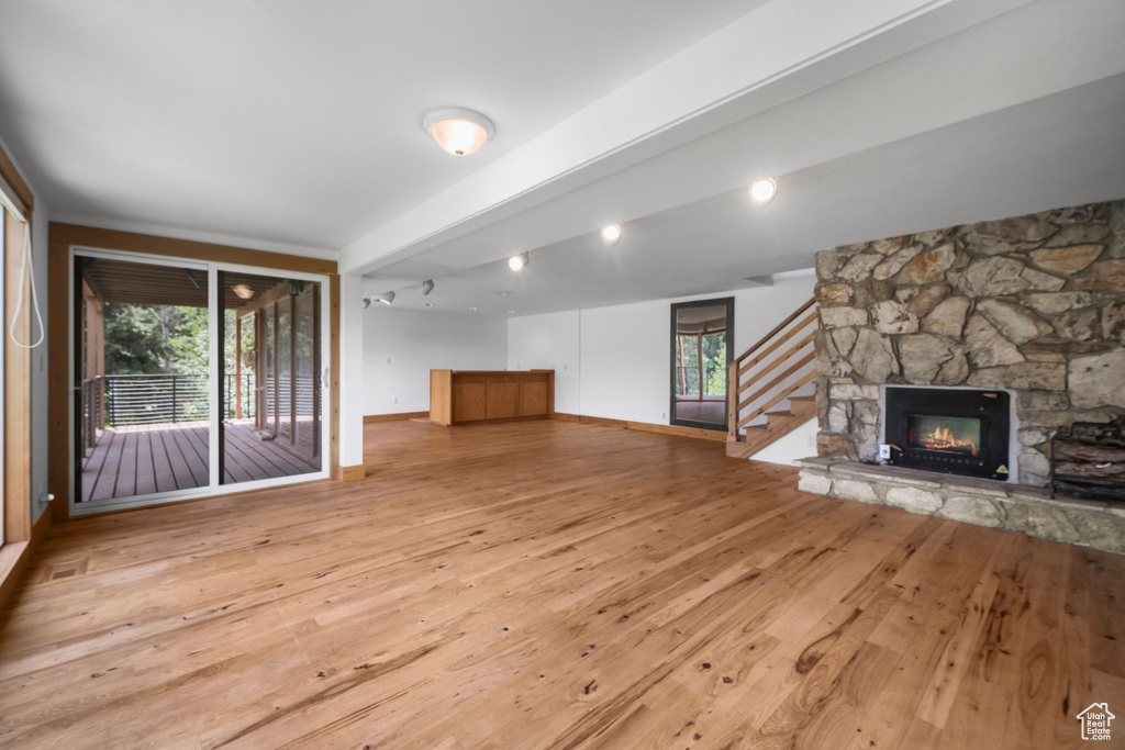 Unfurnished living room with hardwood / wood-style flooring, stairs, a fireplace, beamed ceiling, and baseboards