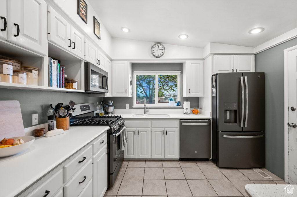 Kitchen with stainless steel appliances, a sink, white cabinetry, light tile patterned floors, and light countertops