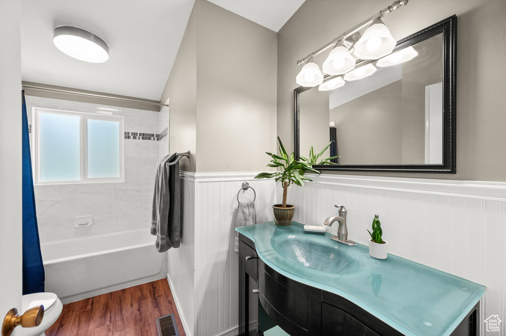 Full bathroom with vanity, shower / bathtub combination with curtain, wainscoting, wood finished floors, and toilet