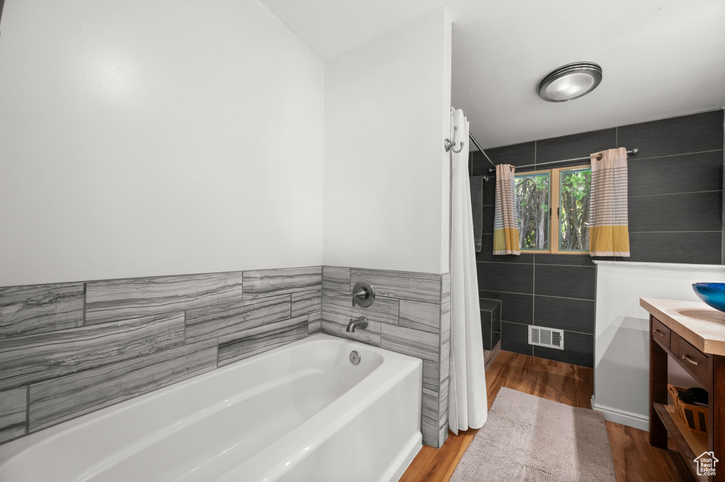 Bathroom featuring vanity, a bath, wood finished floors, curtained shower, and tile walls