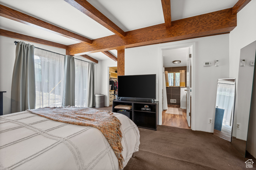 Carpeted bedroom featuring beamed ceiling, ensuite bath, and a walk in closet