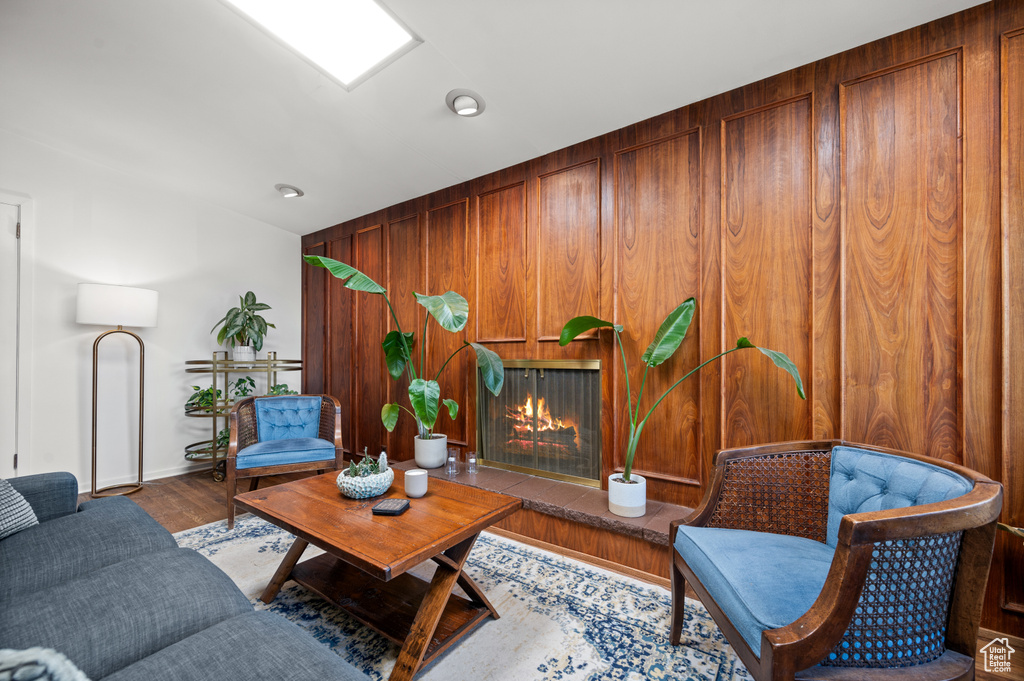 Living room with wooden walls, a lit fireplace, baseboards, and wood finished floors