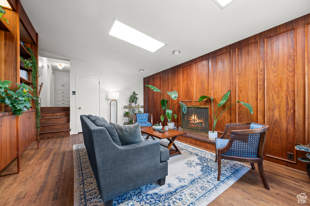 Living room featuring wood finished floors, wood walls, a glass covered fireplace, and stairway