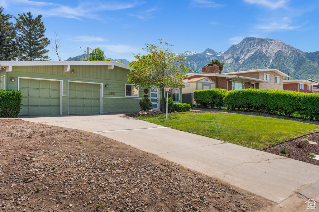 View of front of property with a mountain view, concrete driveway, an attached garage, and a front lawn