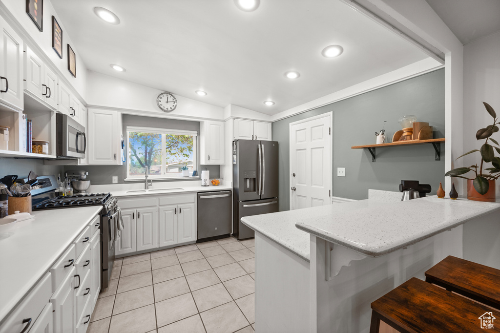 Kitchen featuring stainless steel appliances, a sink, a peninsula, a breakfast bar, and white cabinetry