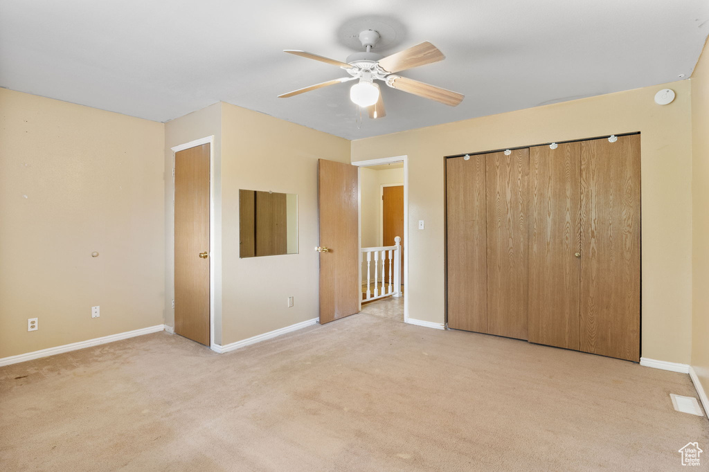 Unfurnished bedroom with baseboards, light colored carpet, a closet, and ceiling fan