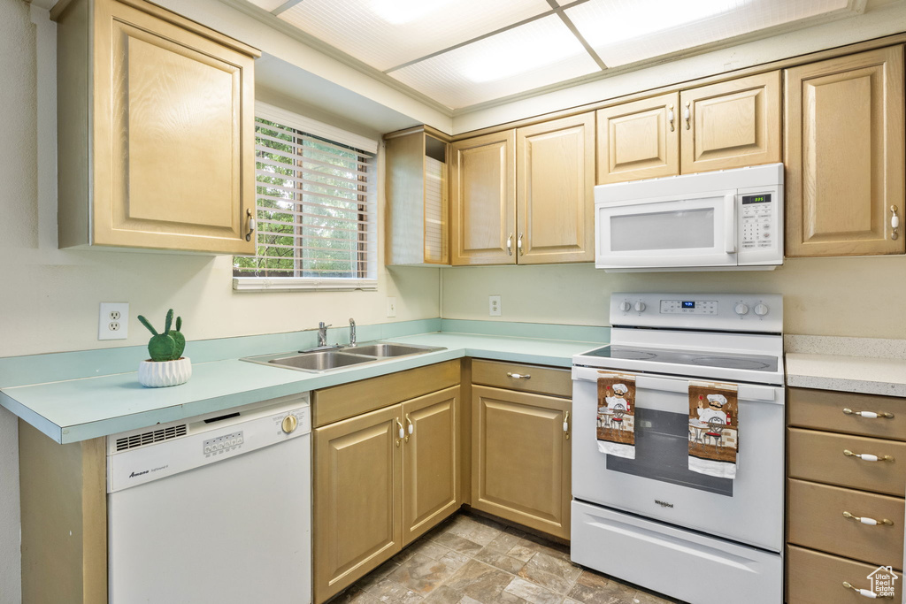 Kitchen featuring white appliances, a sink, light countertops, and light brown cabinets