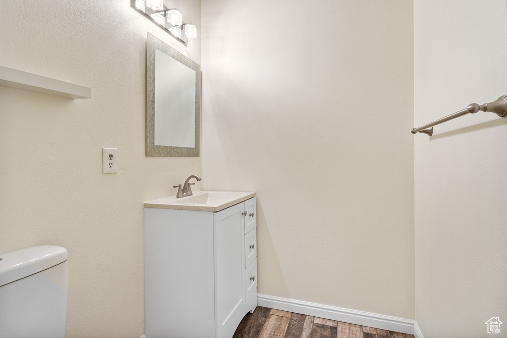 Half bathroom with vanity, wood finished floors, toilet, and baseboards