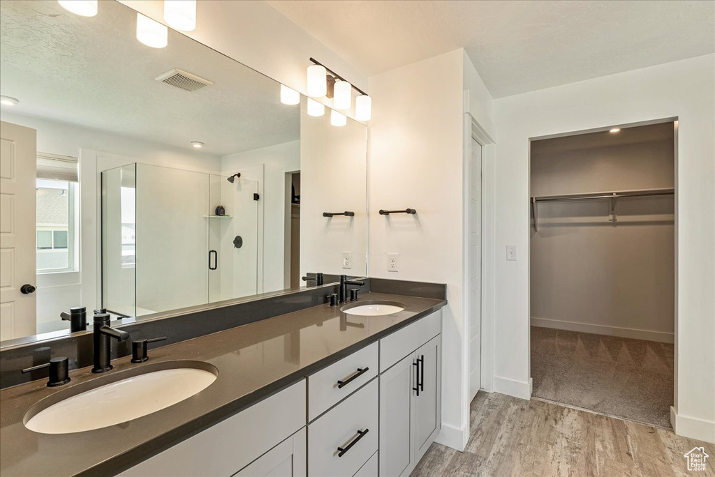 Bathroom with a shower stall, double vanity, a spacious closet, wood finished floors, and baseboards