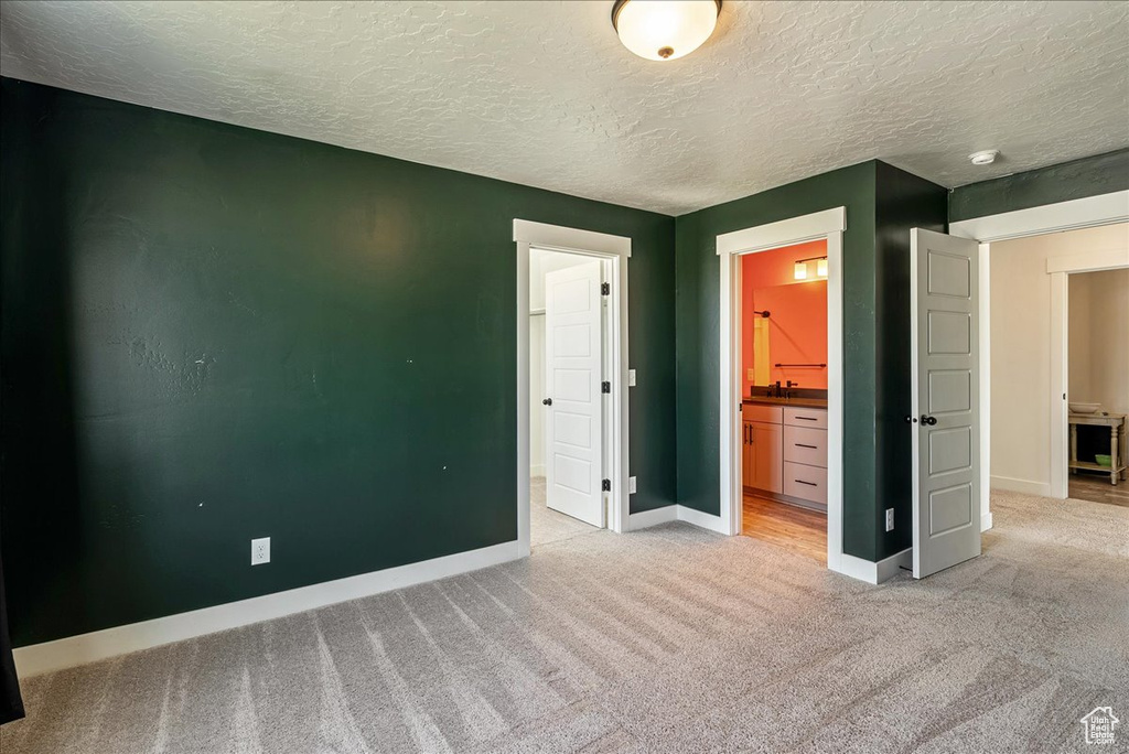 Unfurnished bedroom with light colored carpet, baseboards, a textured ceiling, and connected bathroom
