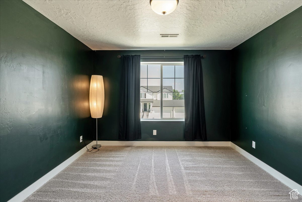 Spare room featuring carpet flooring, a textured ceiling, and baseboards