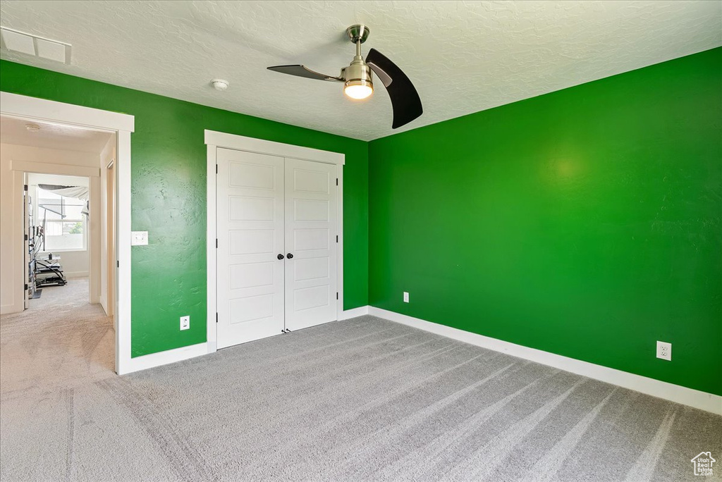 Unfurnished bedroom with carpet flooring, baseboards, a closet, a textured ceiling, and a ceiling fan