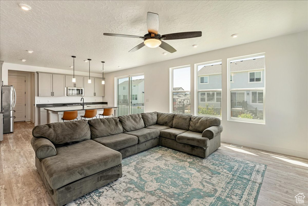 Living room featuring light wood finished floors, a ceiling fan, a textured ceiling, recessed lighting, and baseboards
