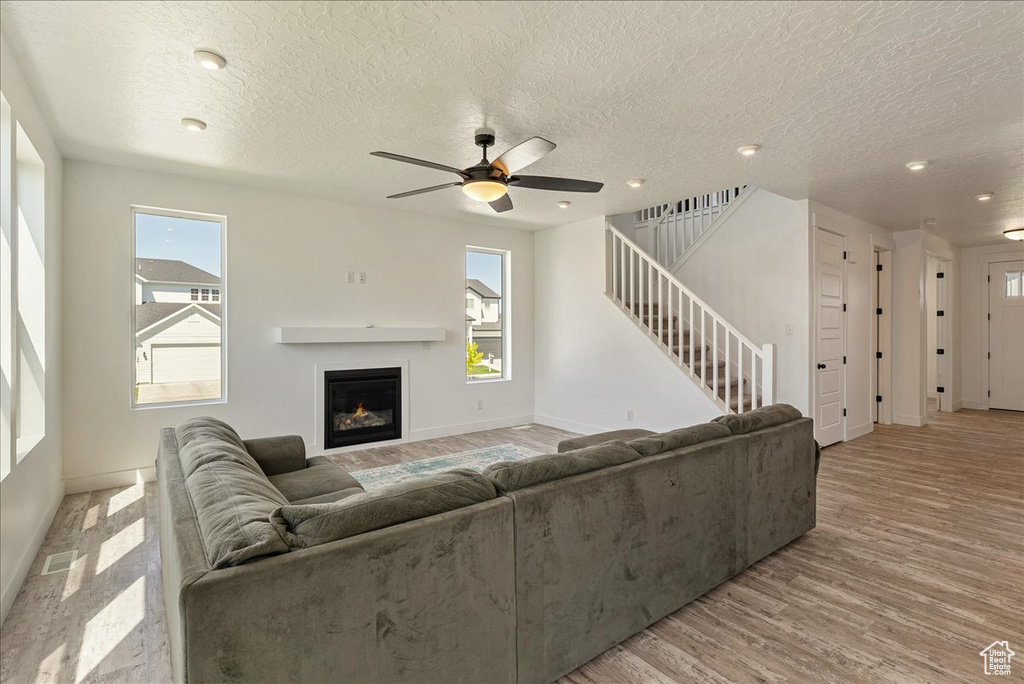 Living room with baseboards, healthy amount of natural light, a ceiling fan, stairs, and a textured ceiling