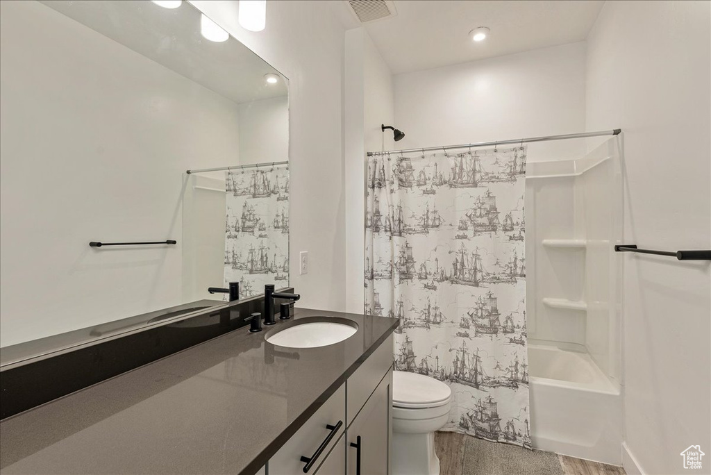 Bathroom with vanity, toilet, shower / bath combination with curtain, wood finished floors, and recessed lighting