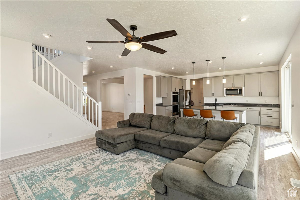 Living room featuring light wood-type flooring, stairs, ceiling fan, recessed lighting, and baseboards